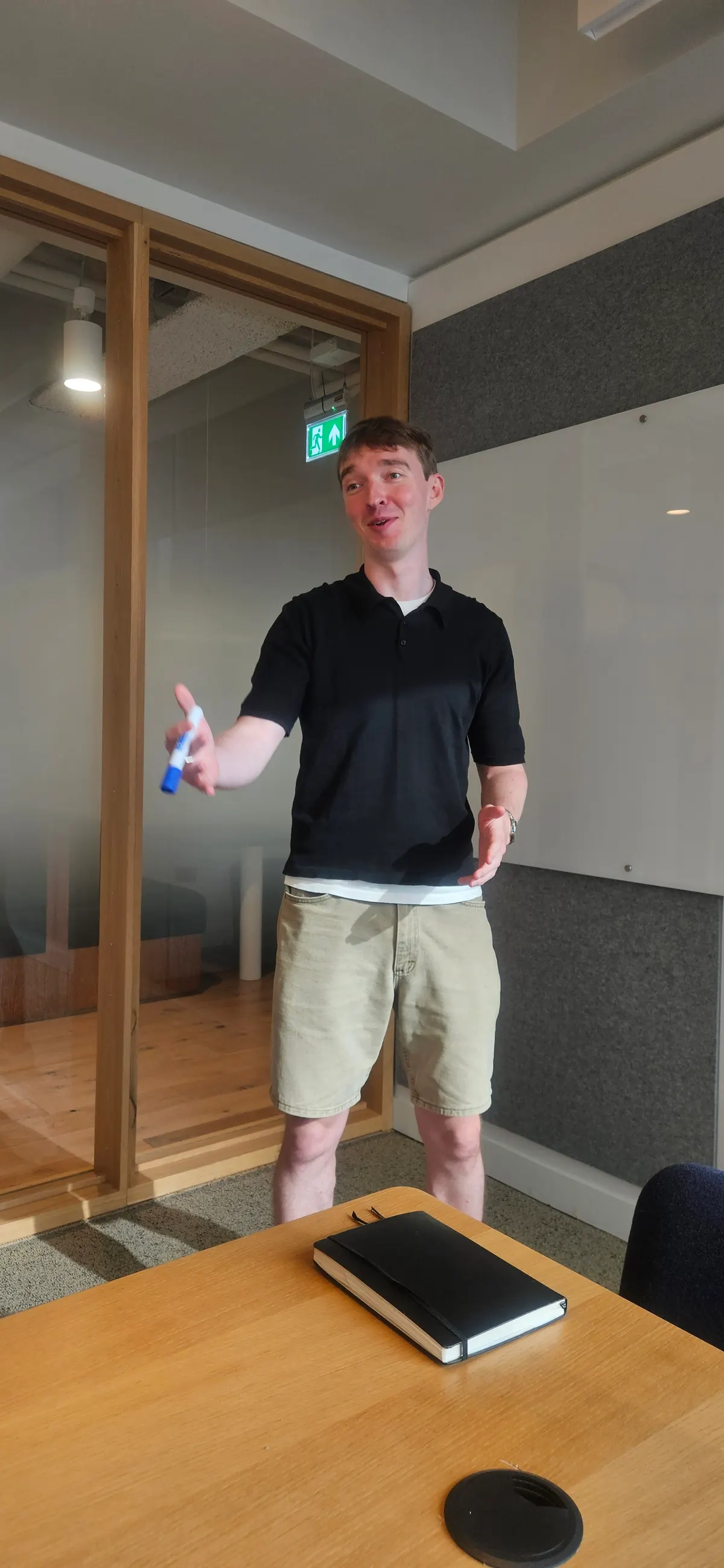 John talking in a meeting room, with a notebook on the table.