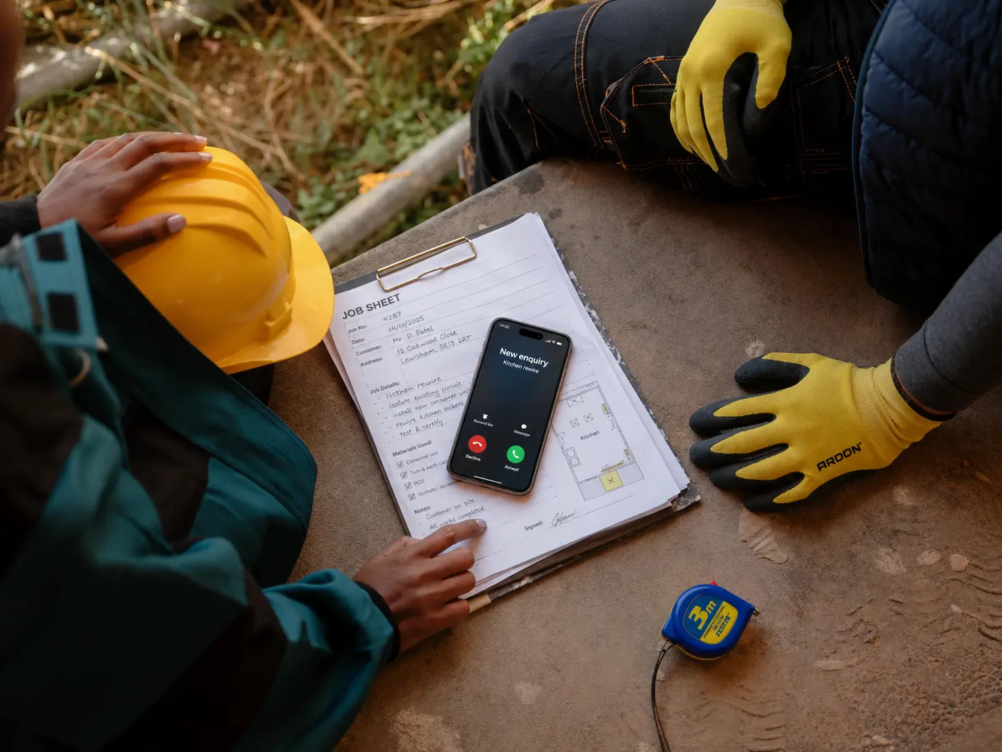 Tradesperson's phone showing an incoming call from a new customer enquiry, lying on a job sheet on site